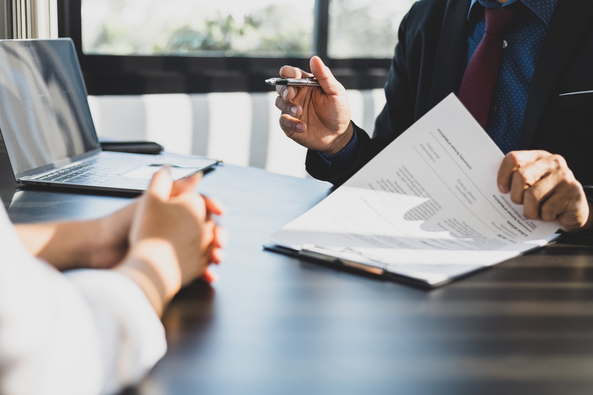 Businessman in suit in his office showing an insurance policy and pointing with a pen where the policyholder must to sign. Insurance agent presentation and consulting insurance detail to customer.